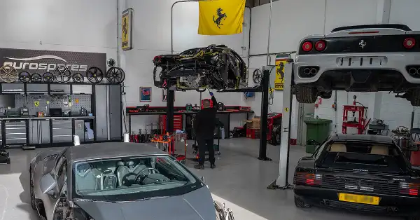 Eurospares technician working on a Ferrari on a workshop ramp with other Ferraris in view.