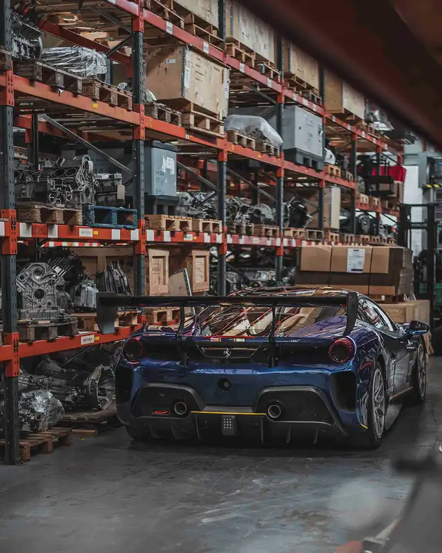 Ferrari Challenge racing car inside the Eurospares engine warehouse, surrounded by shelves stocked with various engine components and parts.